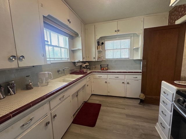 kitchen with white cabinets, decorative backsplash, a sink, and light wood-style flooring