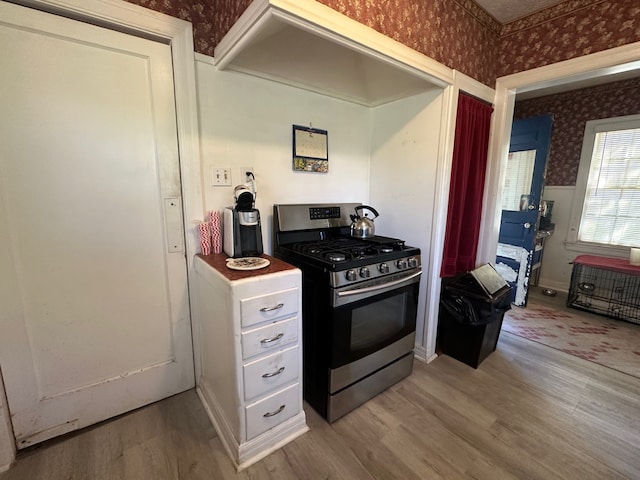 kitchen with light wood-style flooring, white cabinets, stainless steel gas range, and wallpapered walls