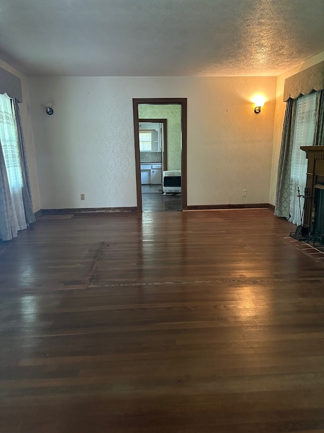unfurnished living room featuring baseboards, a fireplace with flush hearth, a textured ceiling, and wood finished floors