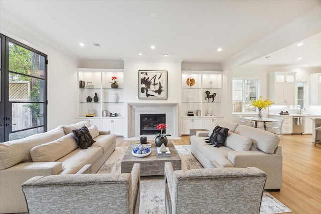 living room featuring a fireplace with flush hearth, recessed lighting, visible vents, light wood-type flooring, and crown molding