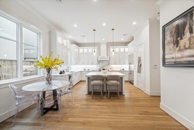 kitchen featuring white cabinets, wall chimney range hood, a sink, a center island, and glass insert cabinets
