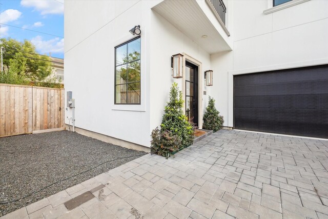 view of property exterior featuring a garage, decorative driveway, stucco siding, and fence