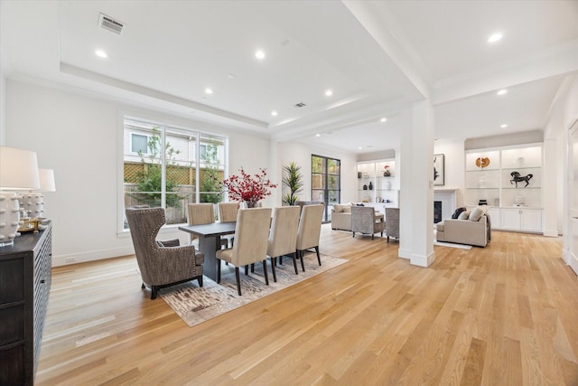dining room featuring a fireplace, visible vents, light wood finished floors, and a tray ceiling