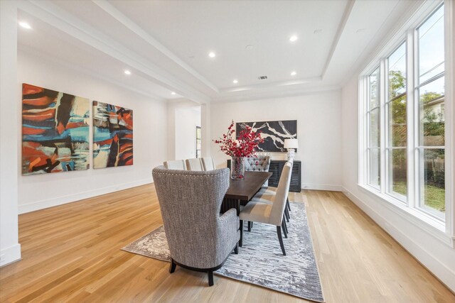 dining area featuring a raised ceiling, light wood-style floors, and a healthy amount of sunlight