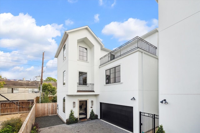 view of front of house with fence, a balcony, stucco siding, an attached garage, and driveway