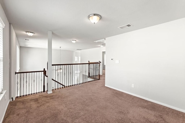 carpeted spare room featuring baseboards, visible vents, and attic access