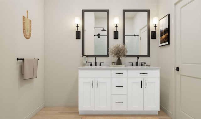 bathroom featuring walk in shower, baseboards, double vanity, wood finished floors, and a sink