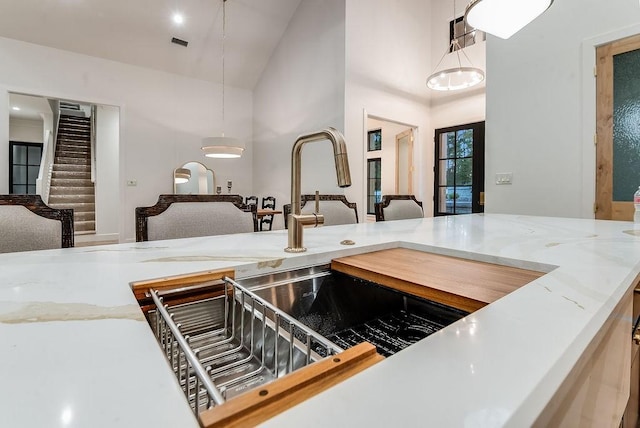 kitchen featuring visible vents, pendant lighting, light stone counters, open floor plan, and a high ceiling