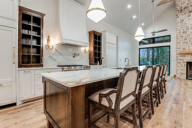 kitchen with premium range hood, a sink, ceiling fan, white cabinets, and light wood-style floors