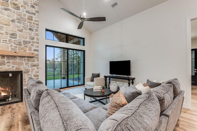 living room with a ceiling fan, wood finished floors, visible vents, high vaulted ceiling, and a stone fireplace