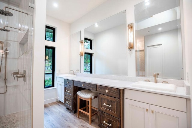 bathroom featuring a sink, tiled shower, wood finished floors, and double vanity