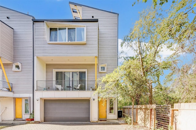 modern home with a garage, a balcony, driveway, and fence