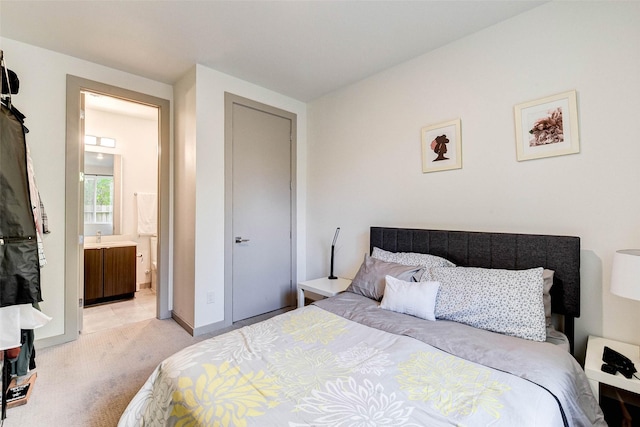 bedroom with light carpet, ensuite bath, and baseboards