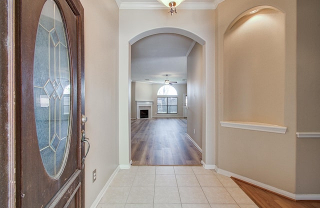 foyer entrance featuring light tile patterned flooring, crown molding, a ceiling fan, a fireplace, and arched walkways