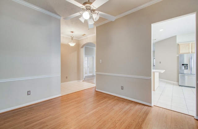 spare room with ornamental molding, baseboards, arched walkways, light wood-style floors, and ceiling fan