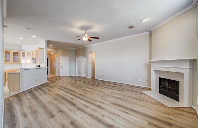 unfurnished living room with light wood-style floors, arched walkways, a tile fireplace, and a ceiling fan