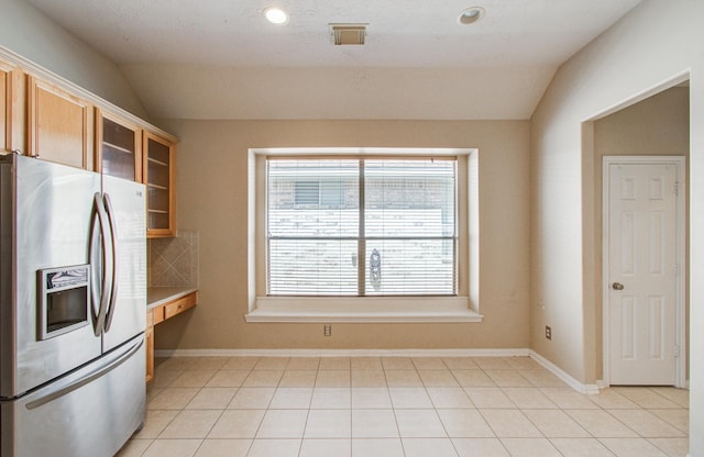 kitchen with stainless steel fridge with ice dispenser, vaulted ceiling, light tile patterned floors, and plenty of natural light