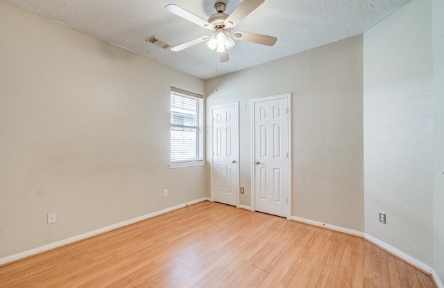 unfurnished bedroom featuring multiple closets, a textured ceiling, light wood-style flooring, visible vents, and baseboards