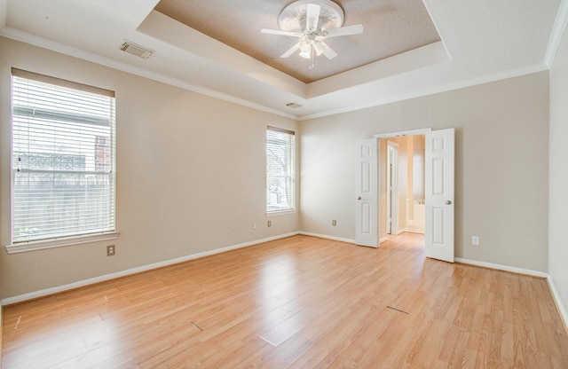 spare room with a ceiling fan, visible vents, a tray ceiling, and light wood-type flooring