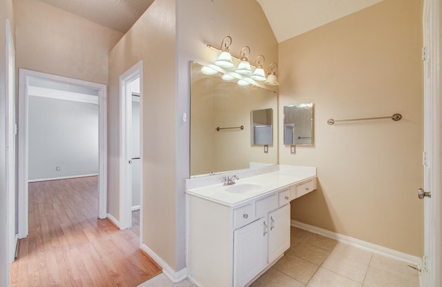 bathroom with baseboards, vaulted ceiling, tile patterned floors, and vanity