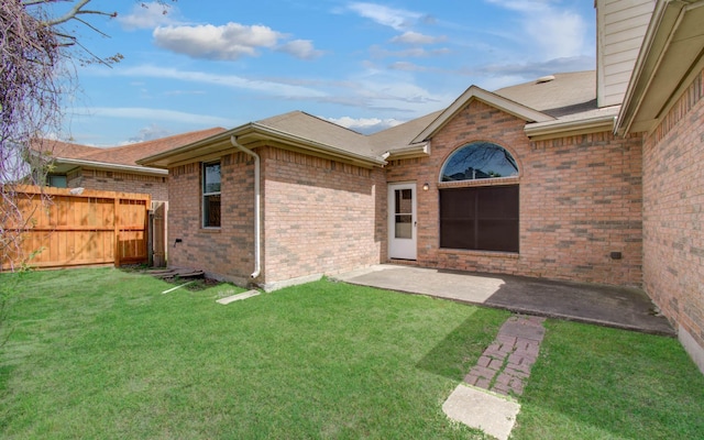 doorway to property with fence, brick siding, a shingled roof, a yard, and a patio area