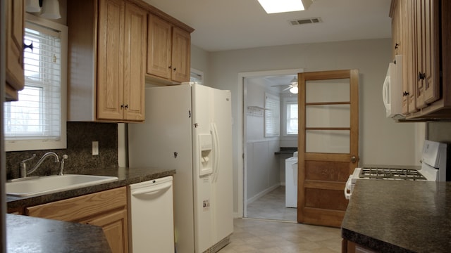 kitchen with visible vents, a sink, dark countertops, white appliances, and light floors