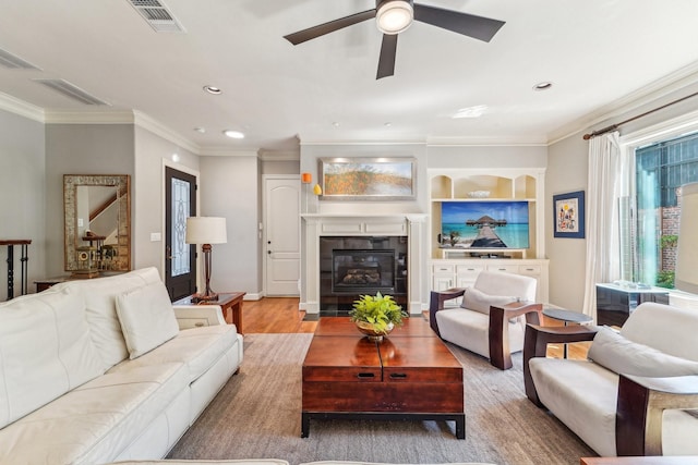 living area with visible vents, ornamental molding, a ceiling fan, a fireplace, and wood finished floors