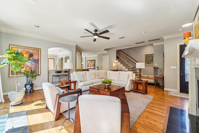 living room featuring stairway, a ceiling fan, visible vents, arched walkways, and wood finished floors
