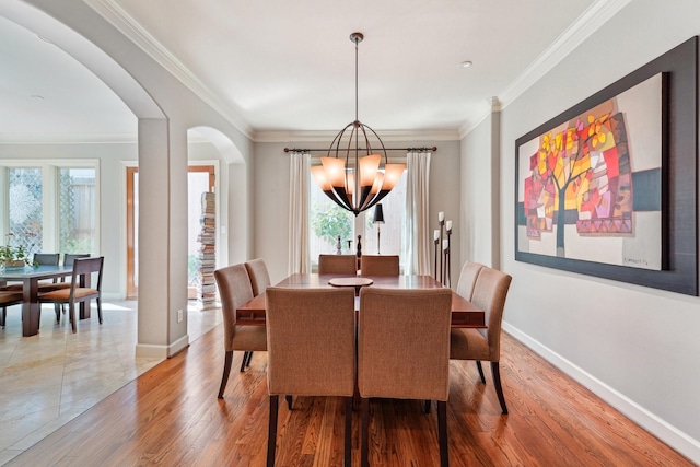 dining room with arched walkways, ornamental molding, wood finished floors, a notable chandelier, and baseboards
