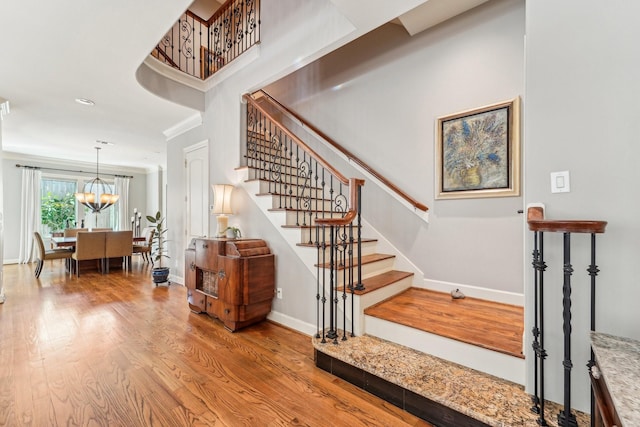 stairs with crown molding, wood finished floors, an inviting chandelier, and baseboards