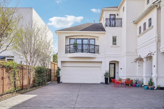 view of front facade with an attached garage, a balcony, fence, stucco siding, and driveway