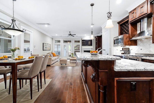 805 Columbia St, Houston, TX 77007 - kitchen with wall chimney exhaust hood, backsplash, ornamental molding, a center island with sink, and a ceiling fan