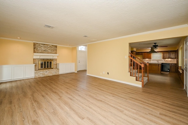 unfurnished living room featuring light wood-style flooring, a textured ceiling, a brick fireplace, and stairs
