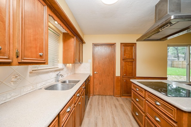 kitchen with wall chimney exhaust hood, brown cabinetry, dishwasher, a sink, and black electric cooktop