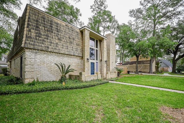 view of side of home with mansard roof, brick siding, and a lawn