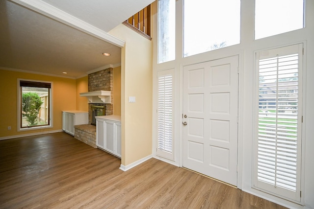 foyer entrance with baseboards, light wood-type flooring, recessed lighting, crown molding, and a brick fireplace