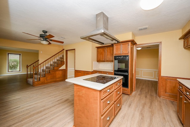 kitchen with light wood-type flooring, island exhaust hood, visible vents, brown cabinets, and black appliances