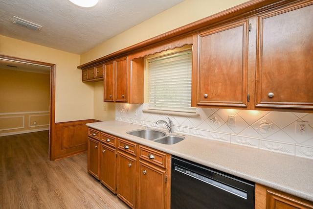 kitchen with light wood-style flooring, visible vents, black dishwasher, a sink, and a wainscoted wall