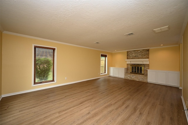 unfurnished living room featuring a textured ceiling, ornamental molding, visible vents, wood finished floors, and baseboards