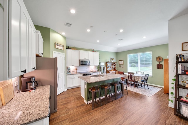 139 Jim Hall Ln, New Waverly, TX 77358 - kitchen featuring stainless steel appliances, a sink, wood finished floors, a center island with sink, and a kitchen bar