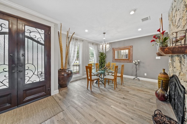 entrance foyer with a notable chandelier, french doors, visible vents, light wood-style floors, and ornamental molding