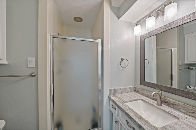 bathroom featuring a textured wall, a stall shower, and vanity