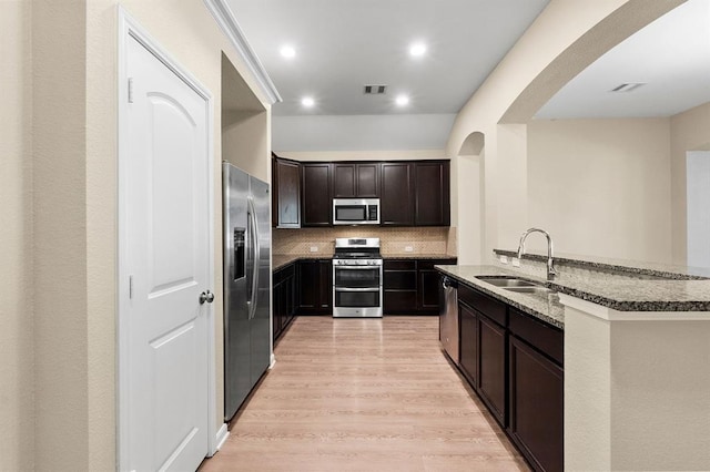 14356 N Summerchase Cir, Willis, TX 77318 - kitchen featuring arched walkways, light wood-type flooring, a sink, dark stone counters, and stainless steel appliances