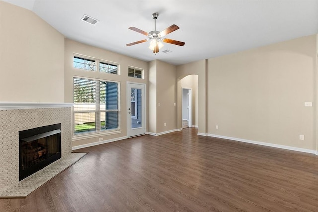 14356 N Summerchase Cir, Willis, TX 77318 - unfurnished living room featuring ceiling fan, visible vents, a tiled fireplace, arched walkways, and dark wood-type flooring