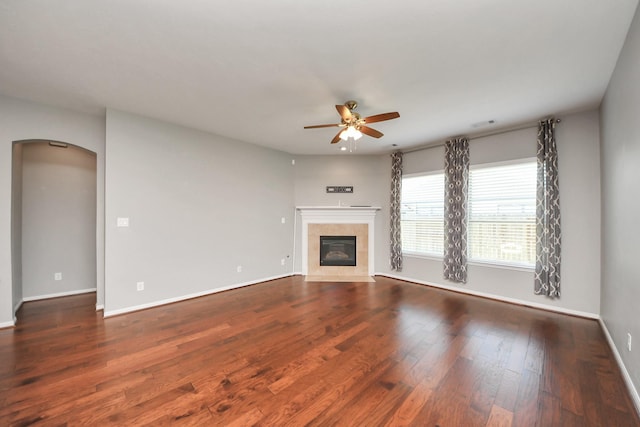 12427 Point Arbor Ct, Tomball, TX 77377 - unfurnished living room featuring arched walkways, a tiled fireplace, baseboards, wood finished floors, and ceiling fan