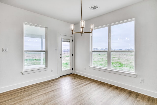 unfurnished room featuring a notable chandelier, visible vents, baseboards, and wood finished floors