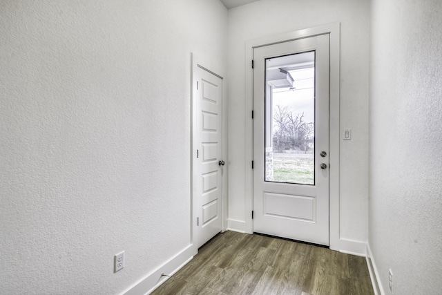 doorway to outside featuring dark wood-type flooring, baseboards, and a textured wall