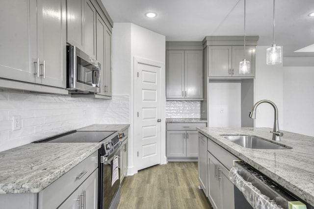 kitchen with light stone countertops, gray cabinetry, stainless steel appliances, and a sink