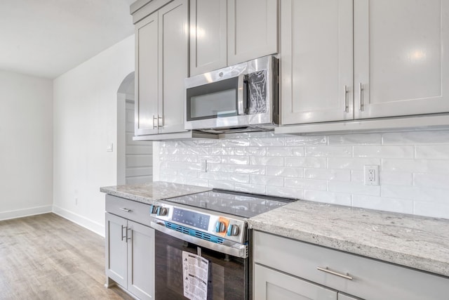 kitchen featuring light stone counters, light wood finished floors, arched walkways, appliances with stainless steel finishes, and tasteful backsplash