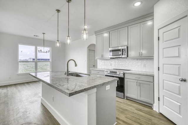 kitchen featuring tasteful backsplash, gray cabinets, stainless steel appliances, and a sink